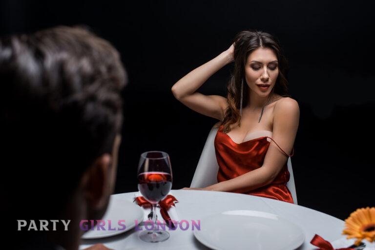 Independent Kensington escort in a red dress enjoying a romantic dinner with a man at a Kensington restaurant.