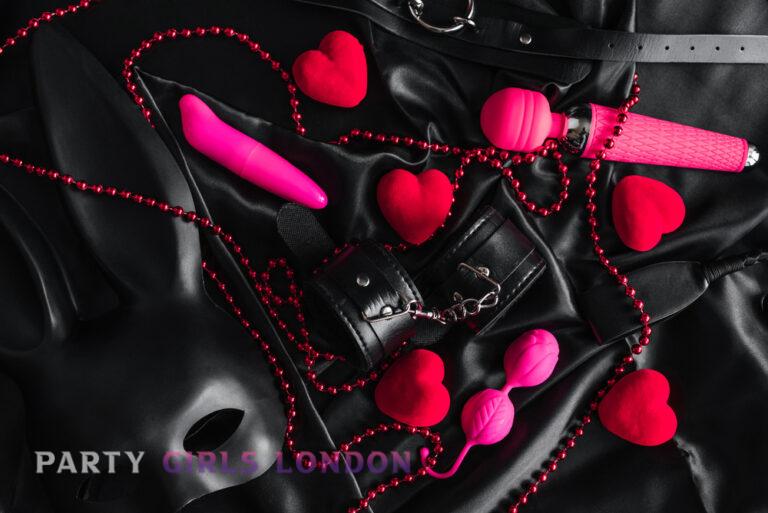 Black satin background with red hearts, leather cuffs, and playful accessories symbolising sensual fantasy and roleplay among London escorts