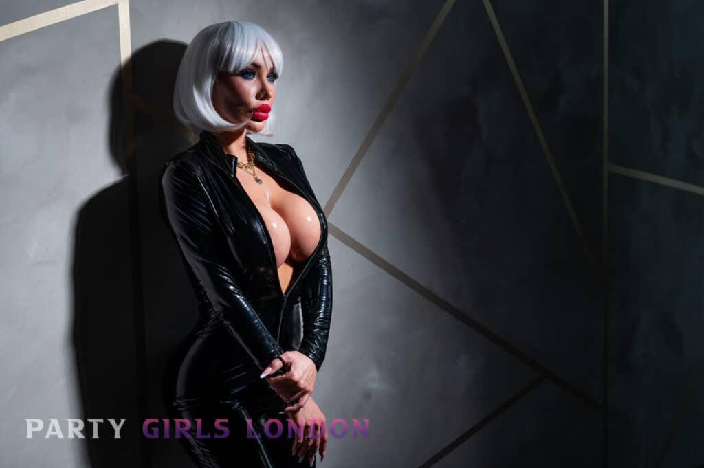 Busty COB escort in London wearing black latex catsuit with platinum blonde wig