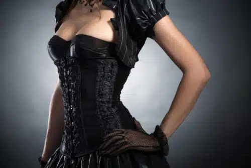 Woman in a black corset and gloves posing confidently in a theatrical Victorian-inspired roleplay outfit